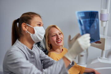 Young female dentist analyzing an x-ray with patient