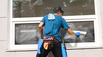 An employee of a professional cleaning service in overalls washes the glass of the windows of the...