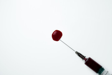 Medical syringe and needle with a drop of blood on a light background