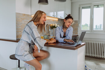 Lesbian couple in pajamas using laptop in the kitchen