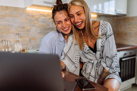 Lesbian couple in pajamas using laptop in the kitchen