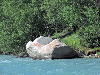 A huge gray boulder in a mountain river. A mountain river with clear blue water. A huge megalithic...