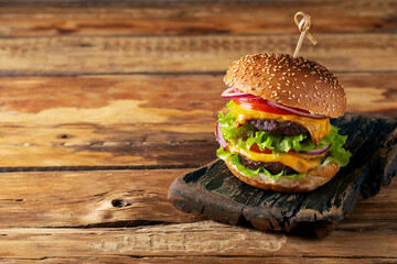 burger with double cutlet and vegetables on a wooden background, place for text