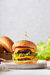homemade burger with two cutlets on a wooden board, greens, cherry tomatoes, beige napkin, vertical
