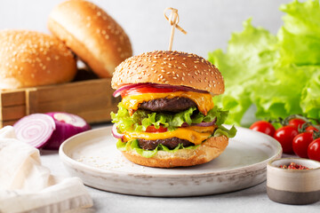 homemade burger with two cutlets on a wooden board, greens, cherry tomatoes, beige napkin