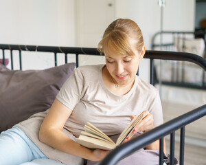 Young woman lying on bed and reading book. Social media detox and gadget free day