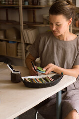 Craftswoman working in pottery workshop
and choosing color for future product from palette