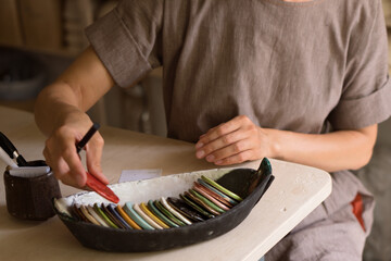 Craftswoman working in pottery workshop
and choosing color for future product from palette