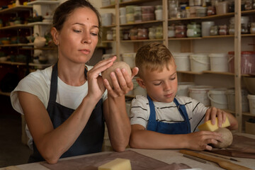 Mother and teenager son spend time together and sculpting from clay in pottery school