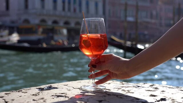 Girl holds in hand and drinks a glass of Spritz, in the city of love - aperitif, alcoholic drink Spritz Camapari or Aperol - typical drink of Venice made with  white wine, orange - Rialto bridg