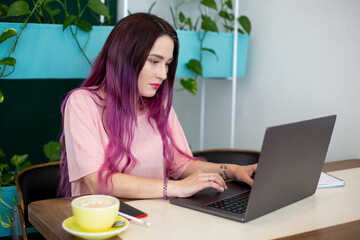 Young woman with pink hair with laptop computer sitting in cafe, intelligent female student working on net-book.