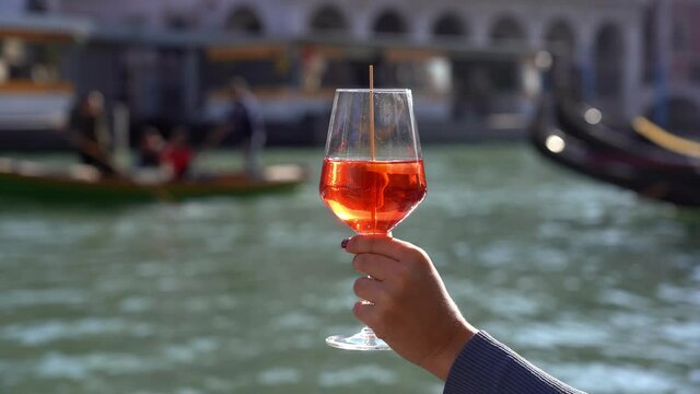 Girl holds in hand and drinks a glass of Spritz, in the city of love - aperitif, alcoholic drink Spritz Camapari or Aperol - typical drink of Venice made with  white wine, orange - Rialto bridg
