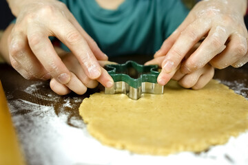 Mom helps the baby cut cookies from the dough. Joint preparation of cookies for the Christmas party. The child prepares food in the kitchen with his mother.
