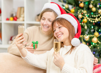 Young girl and her mother wearing Christmas hats, take video calls with friends. Self-isolation. Social distancing during Covid 19 Coronavirus quarantine lockdown