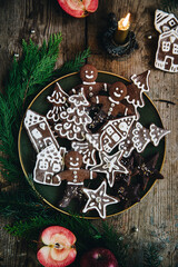 Green plate with shaped homemade gingerbread cookies, hand decorated, with natural Christmas decorations on wooden table.