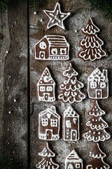 Homemade Christmas gingerbread village with Christmas trees, houses and men sprinkled with icing sugar on rustic wooden table.