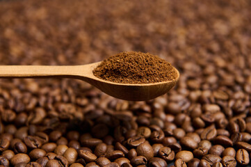 Close-up of a wooden spoon with ground coffee the background of scattered fresh roasted coffee beans with copy space for advertisement. Still life