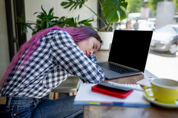 Young woman lying on her arms on the table in cafe in front of laptop with cup of coffee, sleepy.