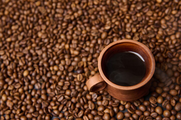 Close-up composition of a clay coffee cup with freshly brewed coffee drink with steam on the background of freshly roasted coffee beans with copy space for ad. Flat lay, high angle view, still life