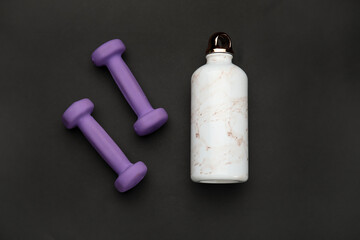 Dumbbells and bottle of water on dark background