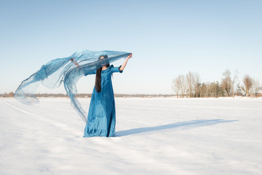 fine art portrait of woman in blue dress standing in cold white snowy winter landscape