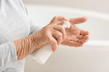 Elderly woman applying cosmetic cream onto her hands in bathroom