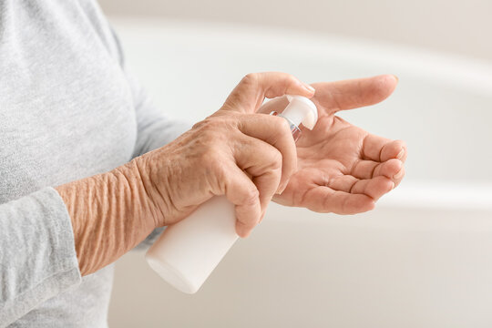 Elderly woman applying cosmetic cream onto her hands in bathroom