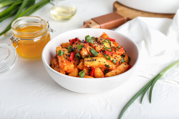 Bowl with honey chilli potato on light background
