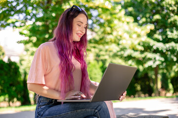 Young girl is studying in the spring park, sitting on the wooden bench and browsing on her laptop