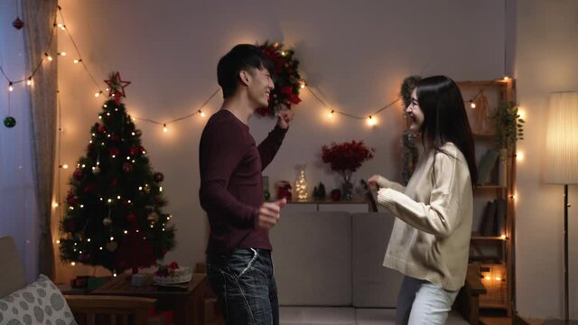 Romance holiday celebration concept. cheerful young asian couple in casual clothing dancing jumping and smiling while standing in living room at home enjoy xmas eve
