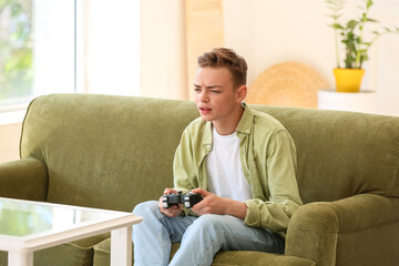 Displeased teenage boy playing video game on sofa at home