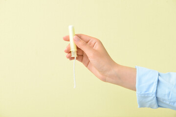 Female hand with menstrual tampon on color background