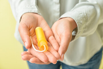 Woman with menstrual tampon on color background, closeup