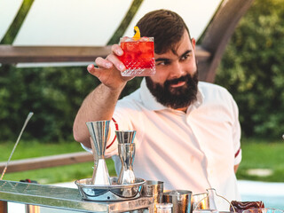 bartender mixing cocktail and drinks outdoors at sunset in a park of a resort