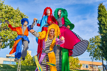 Cheerful harlequins on stilts and unicycle in park during masquerade