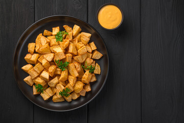 Patatas bravas with sauce and fresh parsley on a black background.