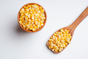 dried corn seeds in wooden bowl and wooden spoon on white background.