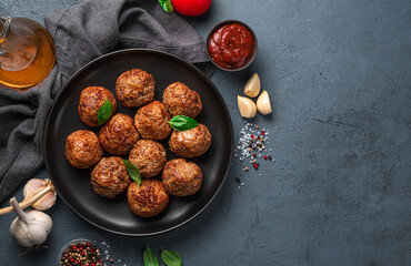 Meat meatballs with basil on a dark background with spices, sauce and garlic.