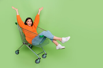 Portrait of attractive cheerful girl riding cart basket fooling having fun isolated over bright green color background