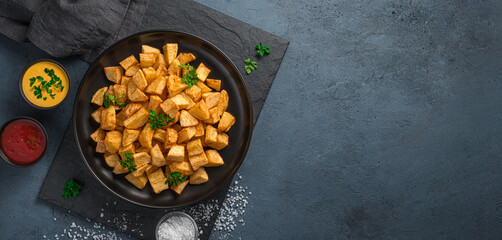 Fried potatoes with salt and sauces on a graphite background.