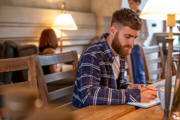 Casual business man or freelancer planning his work on notebook, working on laptop computer with smart phone, cup of coffee on table at coffee shop or home office.