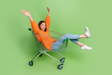 Portrait of attractive cheerful childish girl riding cart having fun isolated over bright green...