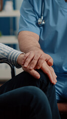 Obraz premium Close up of hands of man nurse comforting senior patient with chronic disability in nursing home. Medical assistant giving support to person sitting in wheelchair. Specialist helping adult