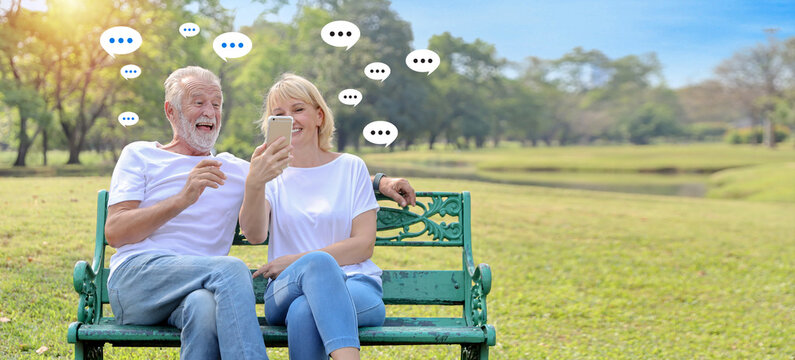 Happy elder caucasian man and woman sitting outdoor using internet on smart mobile phone with social media interaction, notification icons message, comment above device.  Lifestyle with technology. - Powered by Adobe