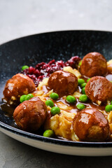 Closeup view of meatballs with gravy served with mashed potato, green pea and cranberry jam