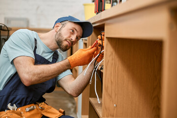 Bearded male electrician repairing desk electrical cable