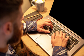 Young man drinking coffee in cafe and using laptop. Man's hands using laptop during coffee break