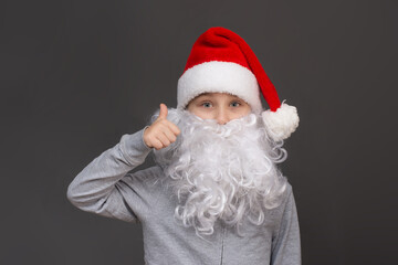 portrait of a boy with a beard and a Santa hat shows class, thumbs up. on a gray background. close -up
