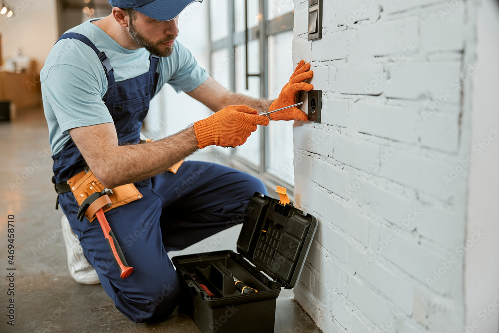 Wall mural male electrician fixing electrical wall socket with screwdriver