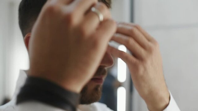 Adult handsome bearded actor in white shirt preparing his hair. Assistant puts powder on face by brush